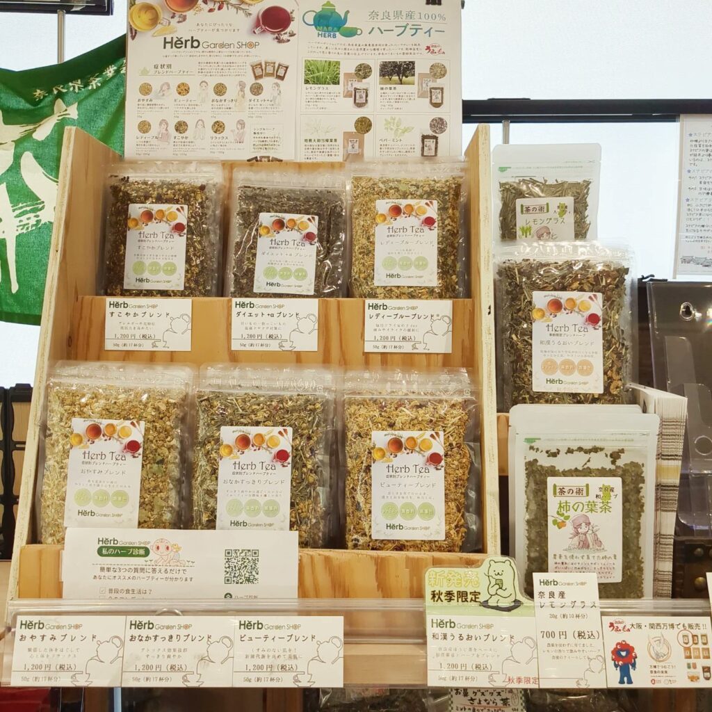 奈良県産100％の柿の葉茶とハーブティー商品が並ぶハーブガーデンショップの店頭棚、季節限定ブレンドやレギュラー商品を展開